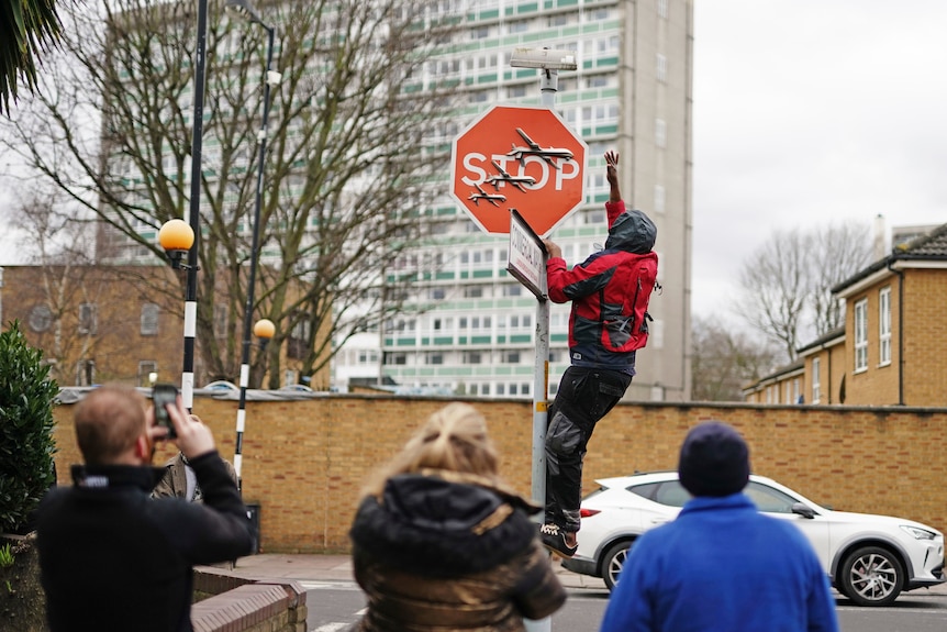 A person climbs on a post to remove a stop sign