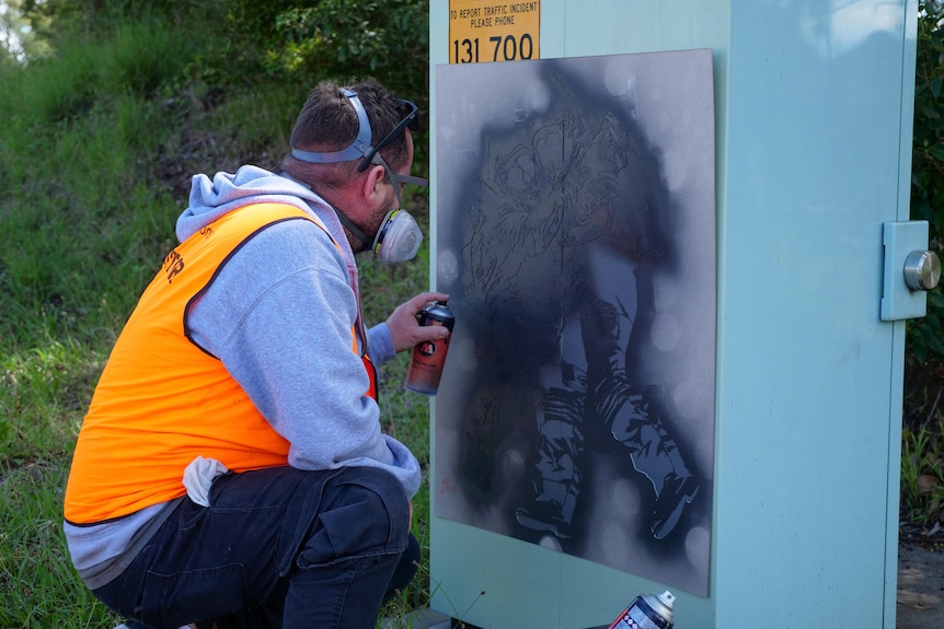 A man spray paints a roadside box.