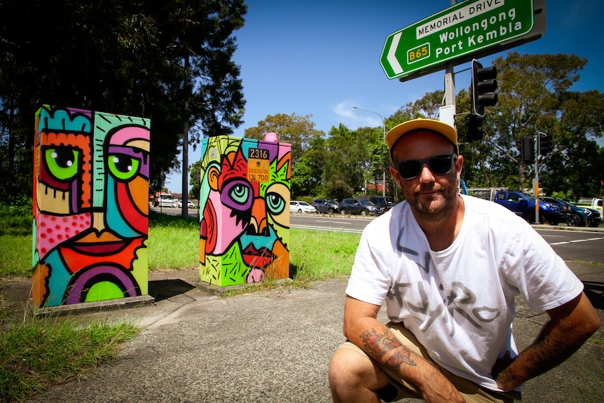 A man stands near two traffic signal boxes he painted in Wollongong.