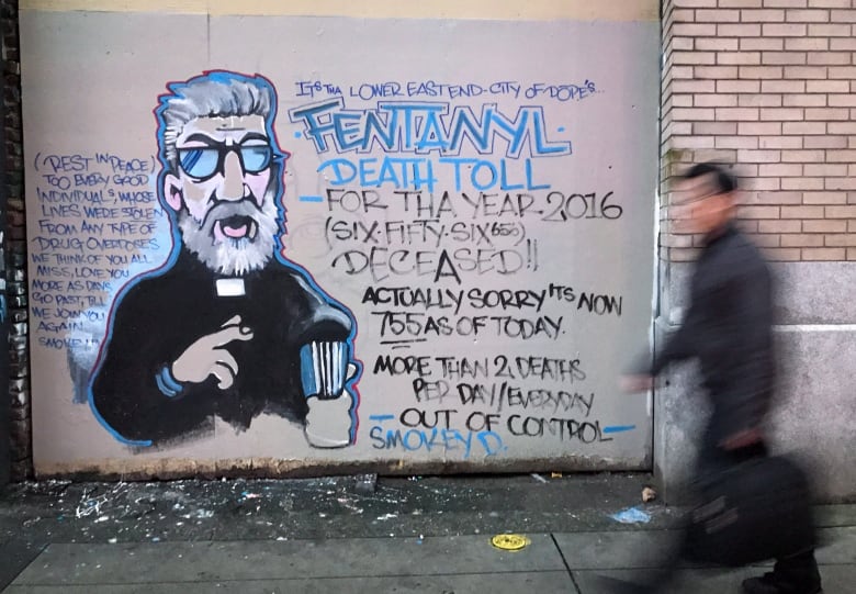 A man walks past a graffiti mural of a preacher with facts about the toxic drug crisis written beside his image.