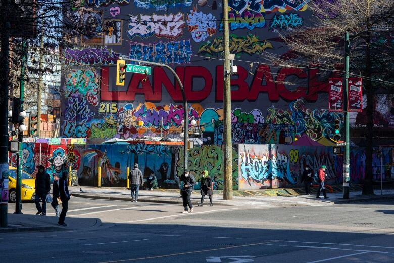 An elaborate mural reads 'LAND BACK' on a parking lot wall.