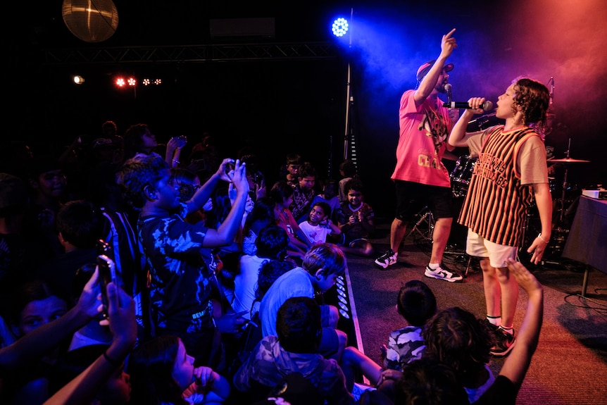 Young boy Inkabee singing into a microphone, on stage with his father Flewnt.