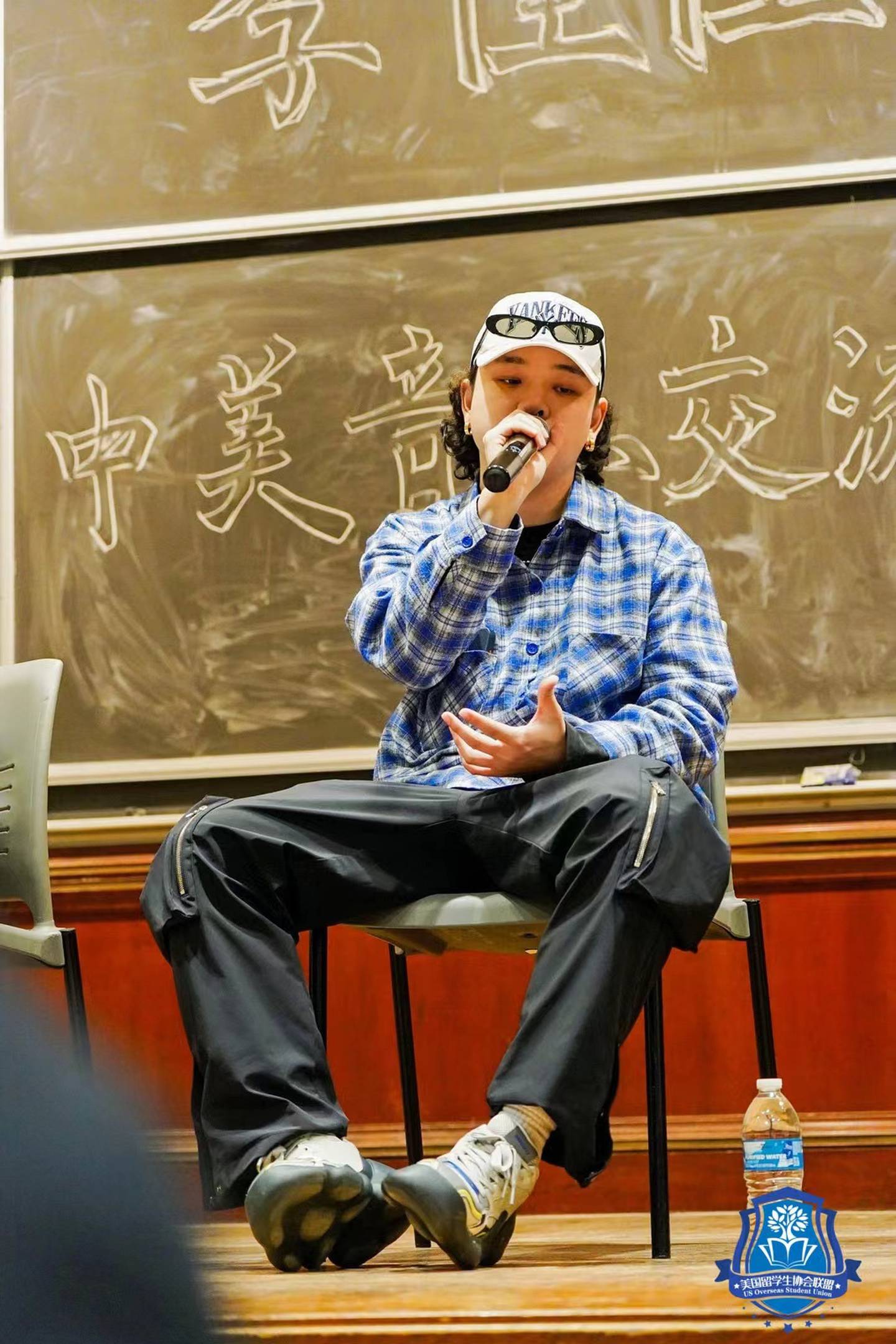 Photo of a man speaking into a microphone in front of a blackboard