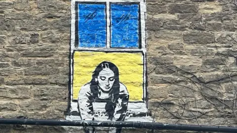 Nadiya Close up of mural showing a lady in a window coloured yellow and blue like flag of Ukraine