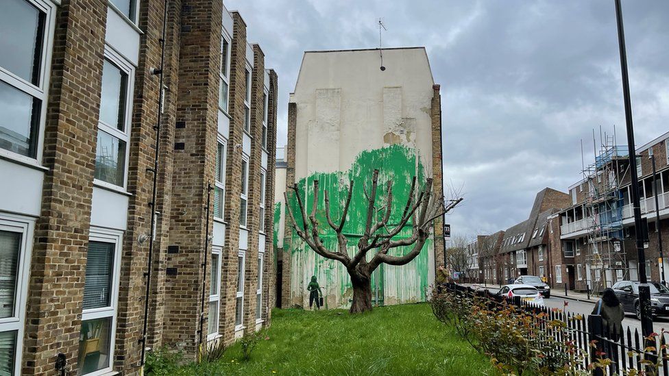 The artwork thought to be a Banksy. A cut back tree stands in front of a mass of green paint on the wall behind