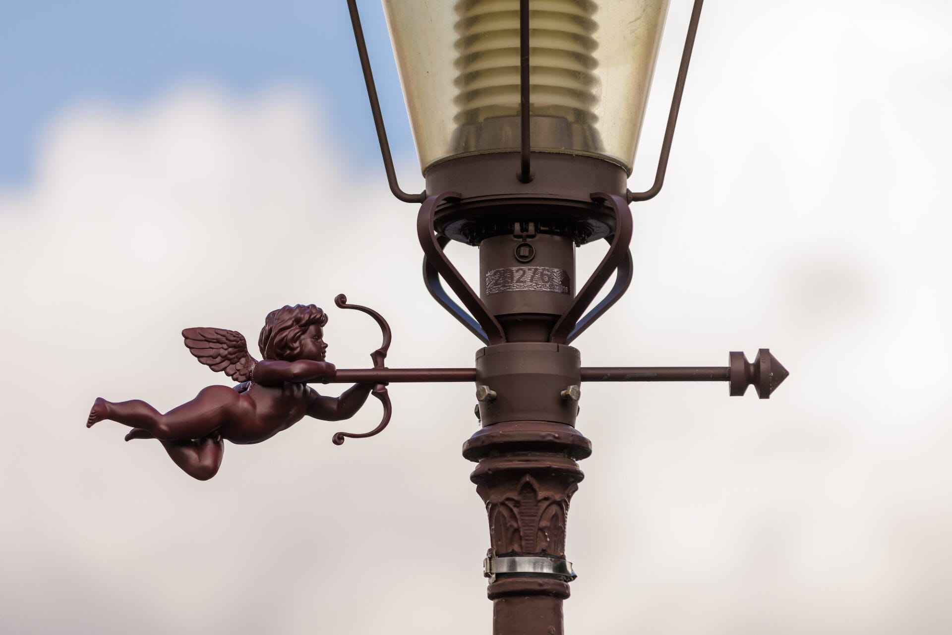 A sculptural intervention on a light post in which a cupid shoots an arrow through the post.