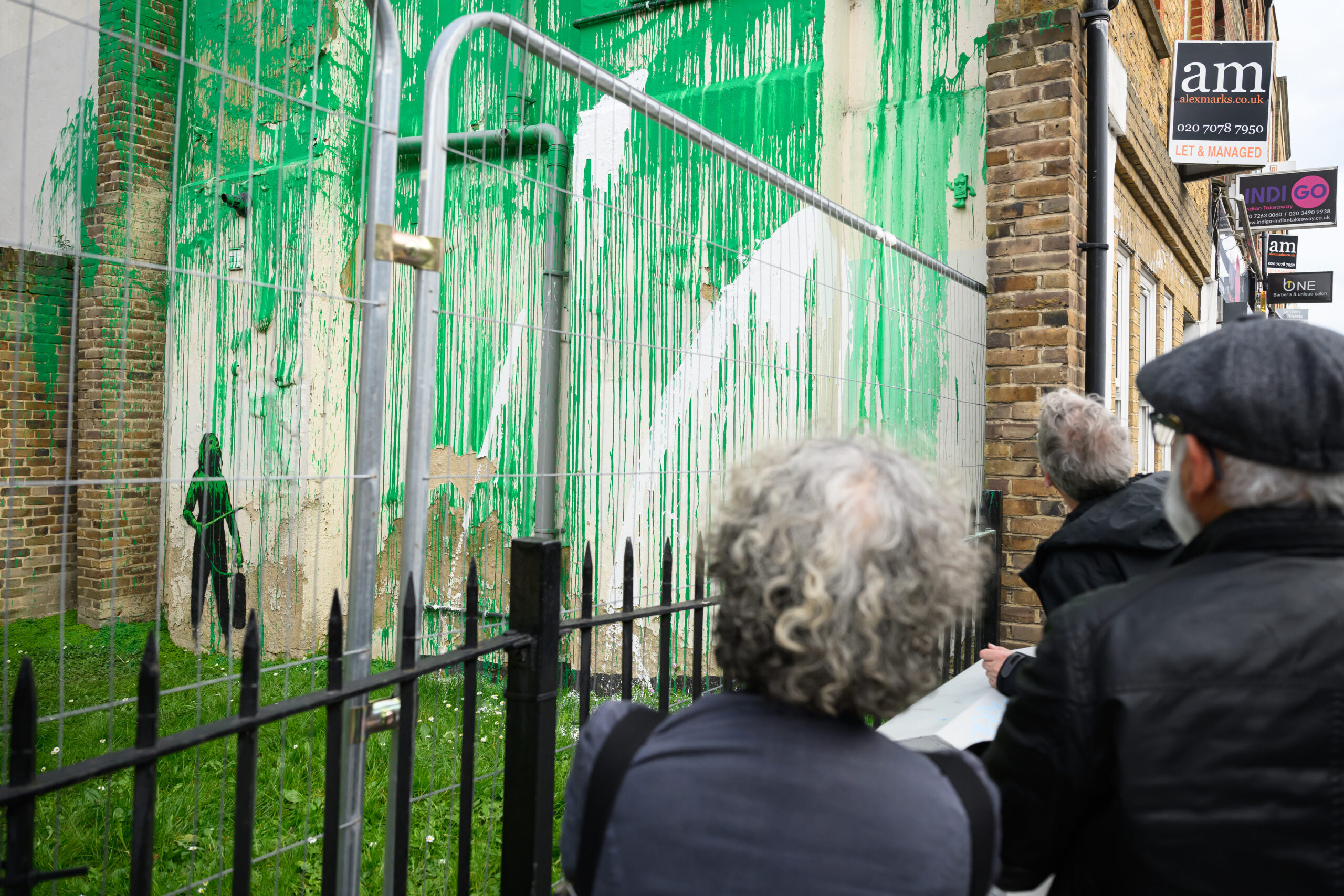 Onlookers view green-painted building with large swaths of white paint thrown on top of it
