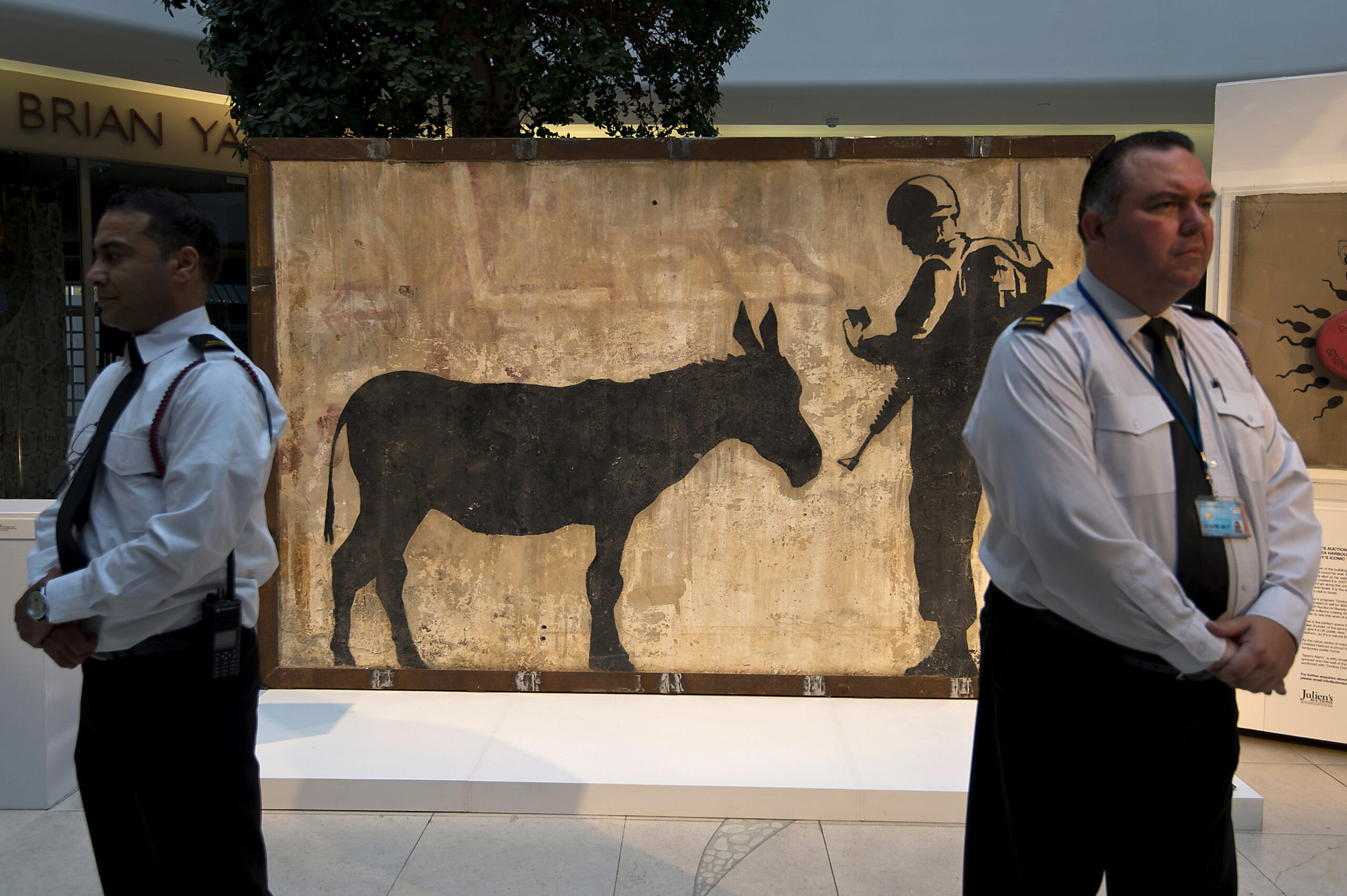 Two security guards stand in front of a mural of a donkey and man