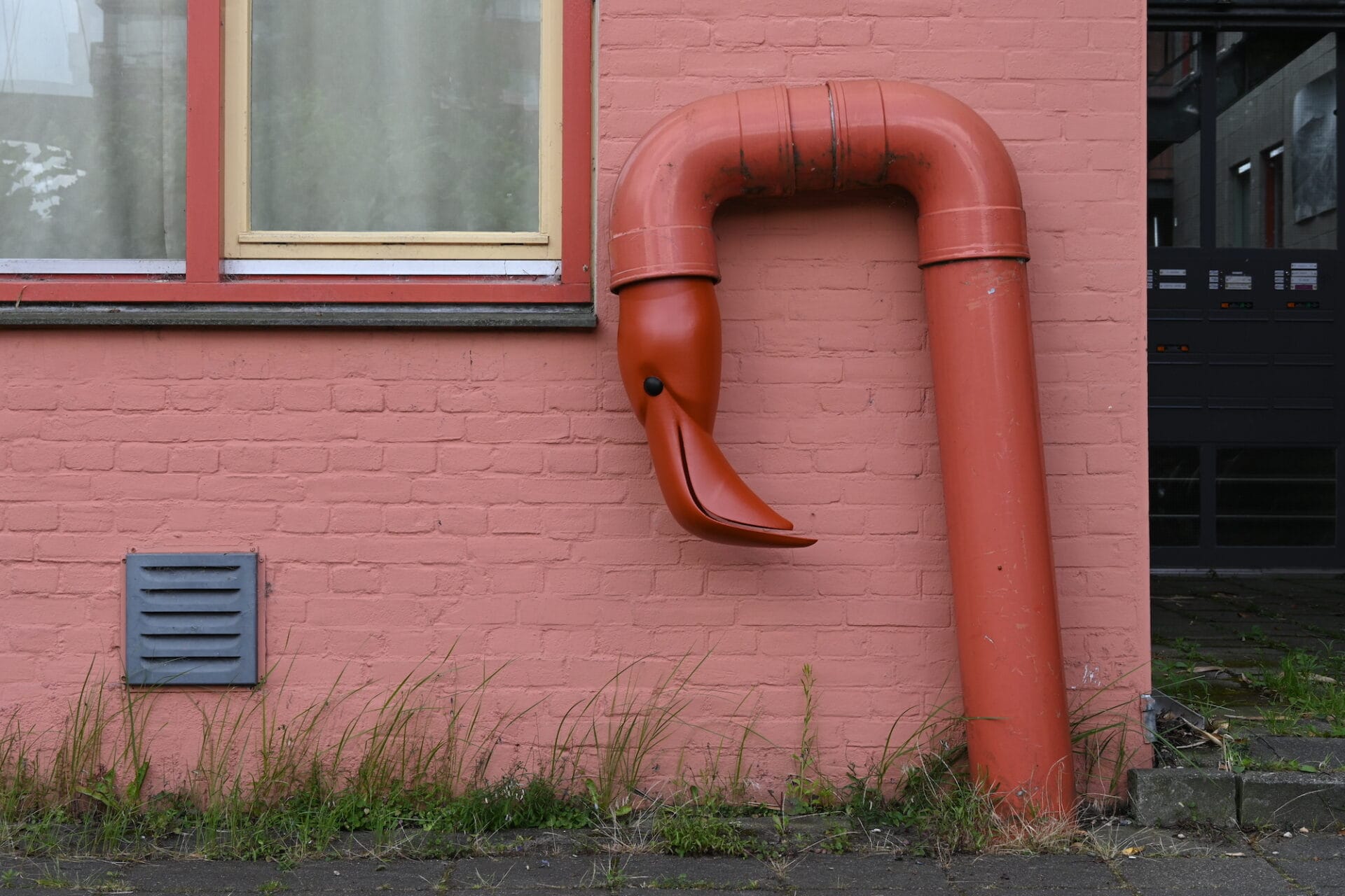 A sculptural intervention on a large pink duct outside, with a flamingo's head stuck in the end of the pipe.