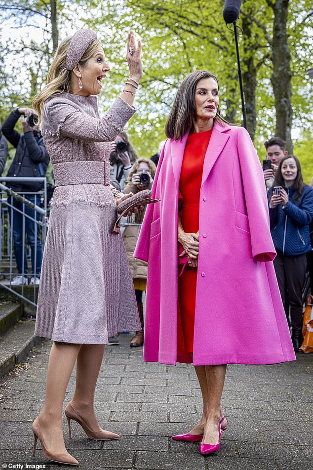 Queen Maxima excitedly waves to someone as Letizia poses for cameras