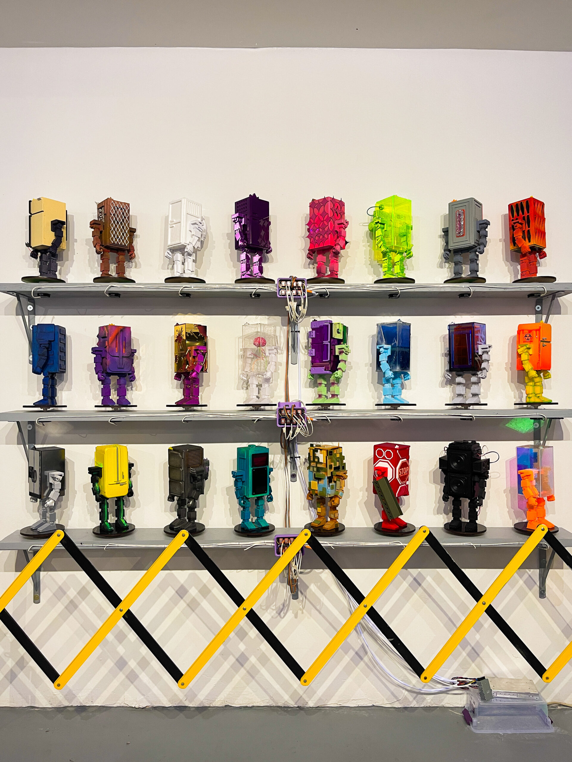 24 robot sculptures mounted on shelves in rows of 8.