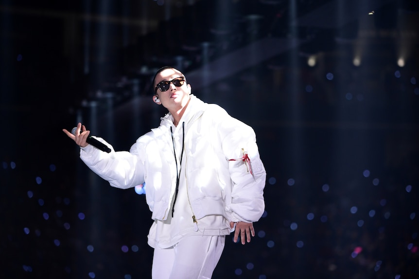 A young Chinese man in white hip-hop-style clothing performs onstage.