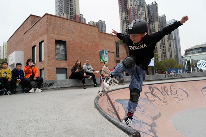 A young Chinese boy skates in a half-pipe as other children and adults watch on.