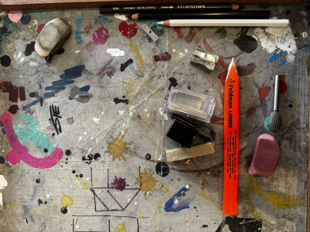 A paint-splattered surface filled with pencils and erasers