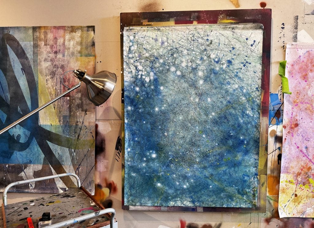 A studio wall hung with a painting splattered with blue paint.