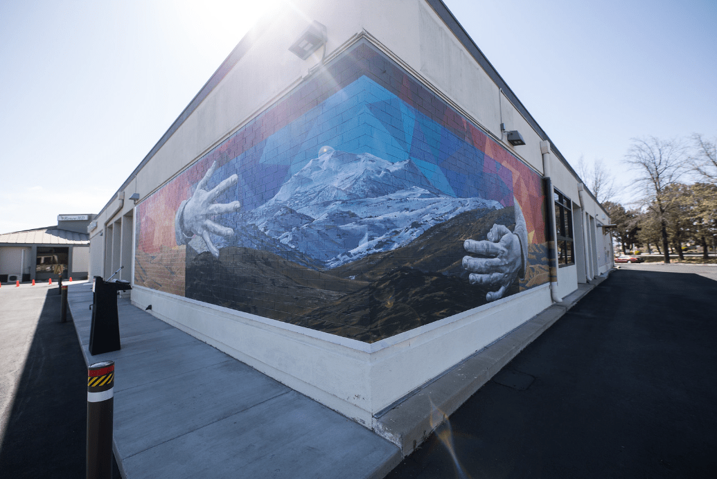Nevada murals. From the corner of a building we can see a long wall mural that goes down either side of the building. It's an image of mountains with giants hands cradling them.
