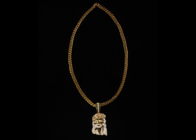A gold chain with a gold-and-diamond pendant of Jesus's face, against a black background.