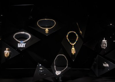 View of several pieces of jewelry designed for hip-hope artists. Tehy are all shown on black velvet stands in a display case.
