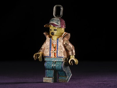 A Lego pendant, made of 14-karat gold with multicolored diamonds, sapphire, ruby, and enamel. He is shown mid-stride on a purple carpet and black background.