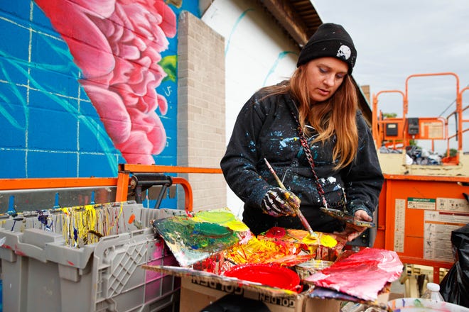 Nico Cathcart of Toronto dips her brush into paint for her mural on the side of the ZStone Creations building at 711 S. Main St. during Mural Mania on Friday, July 5, 2024, in South Bend. This year marks South Bend's third Mural Mania where artists from around the world paint murals across the city at the same time.