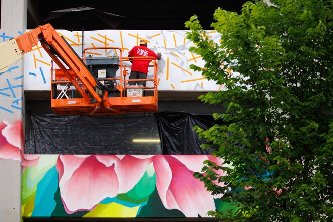 Max Sansing spray paints the side of the Main & Colfax garage during Mural Mania on Friday, July 5, 2024, in South Bend. This year marks South Bend's third Mural Mania where artists from around the world paint murals across the city at the same time.