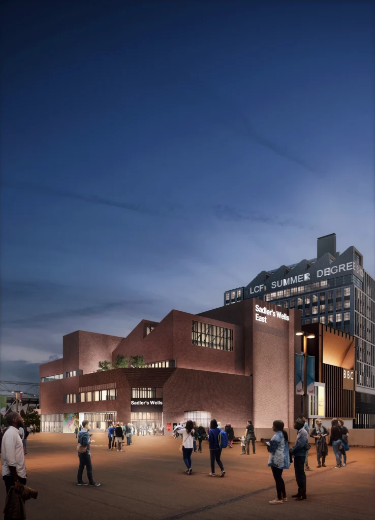 A digital rendering of Sadler's Wells East shows a brown-brick building at twilight, angular windows shedding light into the open plaza before it.