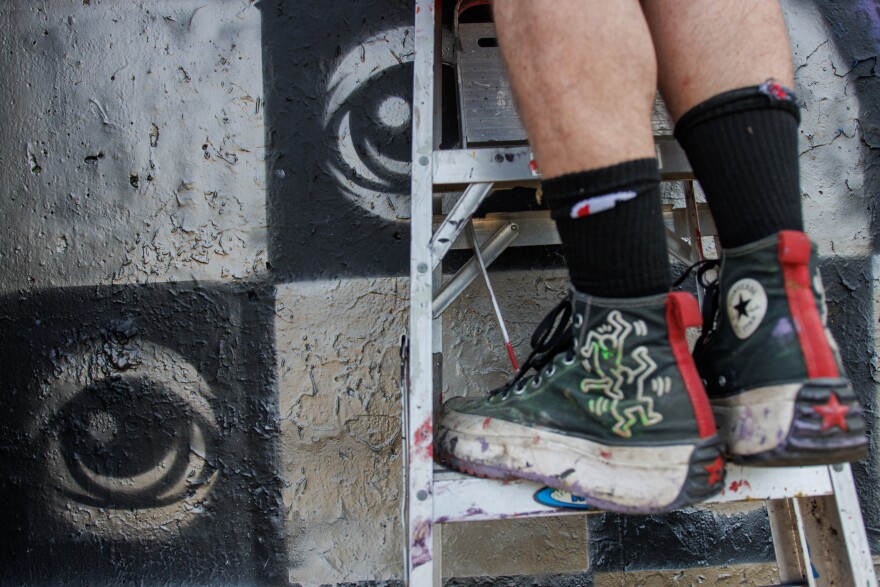 Peat Eyez, from St. Louis, spray paints over his stencils of eyes along the Mississippi River on Friday, August 30, 2024. Peat goes by “Eyez” has been displaying his art is 2000. “A lot of my work is about having a symbol of people being seen… having a third eye and putting eyes out on the street” says Eyez.