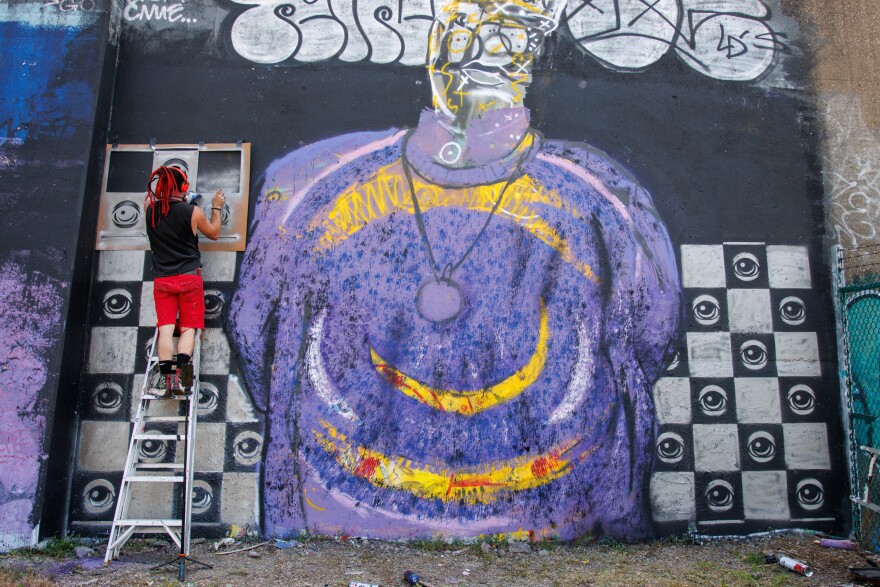 Peat Eyez, from St. Louis, spray paints over his stencils of eyes along the Mississippi River on Friday, August 30, 2024. Peat goes by “Eyez” has been displaying his art is 2000. “A lot of my work is about having a symbol of people being seen… having a third eye and putting eyes out on the street” says Eyez.