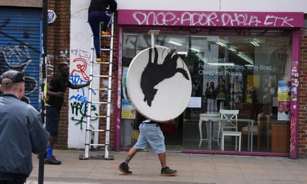 A satellite dish bearing a Banksy wolf silhouette is carried away in Peckham