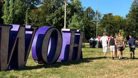 BBC Festivalgoers walking past a large freestanding purple WOH sign