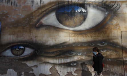 A woman walks in front of a mural of a large brown eye, surrounded by many smaller versions in a sea of eyes