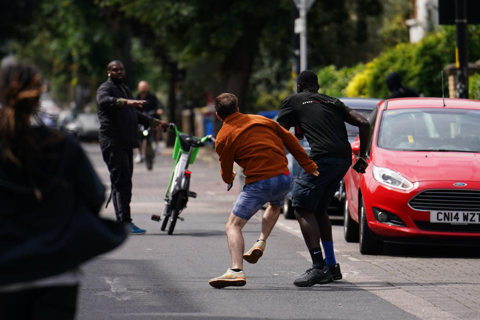 Tom Kellow (orange jacket) chases the people who removed a new artwork by Banksy, depicting a howling wolf painted on a satellite dish that was placed on a shop roof in Peckham, south London. The artist's latest artwork comes a day after he unveiled three monkeys painted on a bridge in Brick Lane, east London. Picture date: Thursday August 8, 2024. PA Photo. See PA story ARTS Banksy. Photo credit should read: Jordan Pettitt/PA Wire