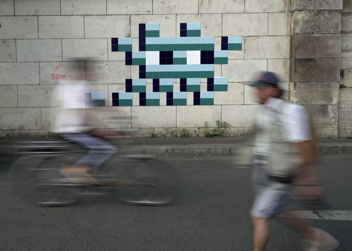 A cyclist rides in front of an Olympic-themed new mosaic by the mysterious on the banks of the River Seine by French street artist known only by the name Invader.