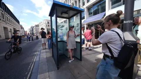 PA Media Woman having her photo taken inside the police box where the windows have been painted by Banksy