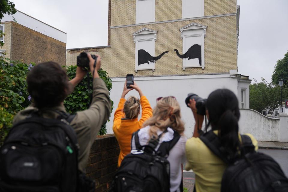 People photograph the Banksy depicting two elephants poking their heads out of blocked-out windows (PA Wire)