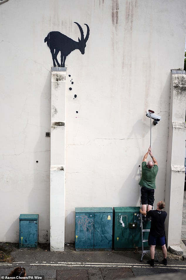 Employees move a CCTV camera back to its original position after Banksy moved it