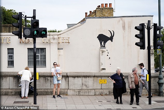 People look at the new Banksy piece of artwork near Kew Bridge of a goat on a wall yesterday