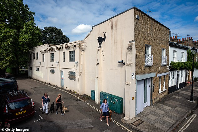 Women walk dogs past a mural depicting a goat by the street artist Bansky in Kew Bridge