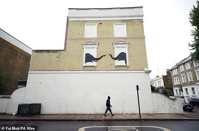 A man passes under the new artwork unveiled by Banksy on the side of a building in Chelsea