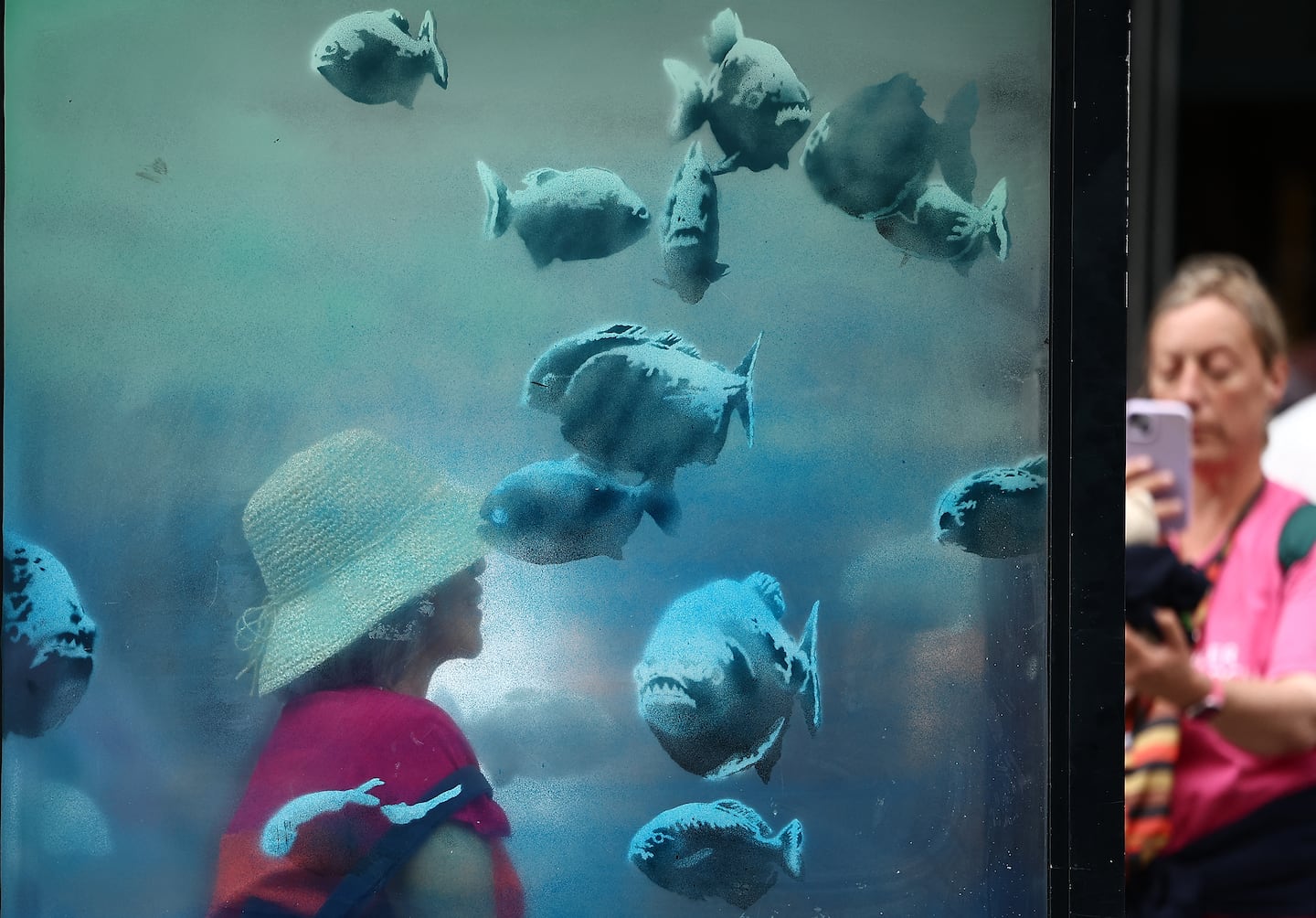 A person poses for a photograph with an artwork by street artist Banksy, the seventh to released this week, depicting piranha fish swimming around a Police Box, in the City of London, on August 11, 2024.