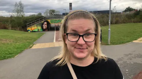 John Devine/BBC Samantha Johnson is 31, she has blond shoulder length hair, swept back with a black hair band. She is wearing dark rimmed glasses and has the strap of a bag across her shoulder and is wearing a black top