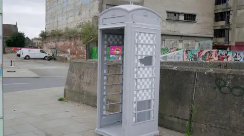 Wild Walls Festival/Joe Barton A telephone box in Ipswich painted grey with a chequered paint design over its class windows.