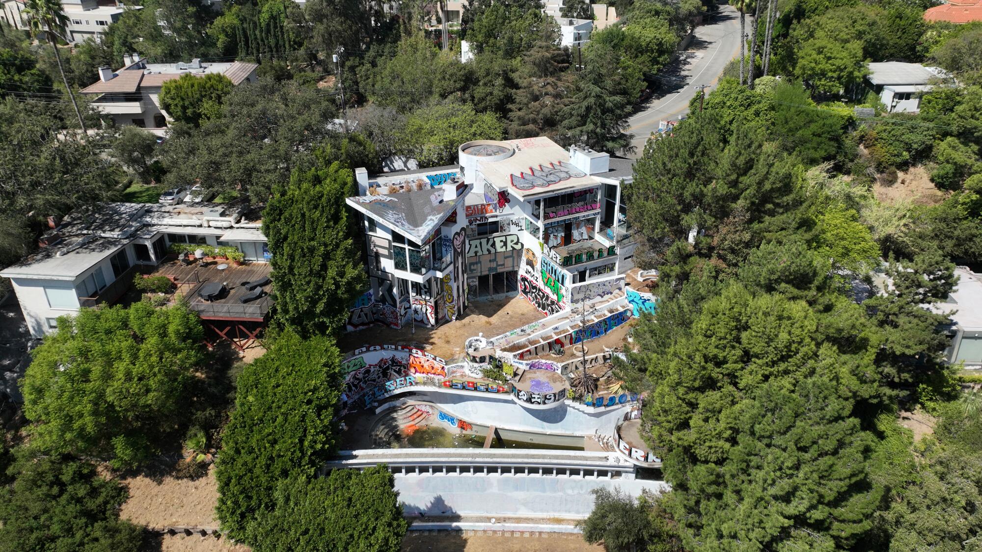 Aerial view of graffitied mansion surrounded by trees and other homes.