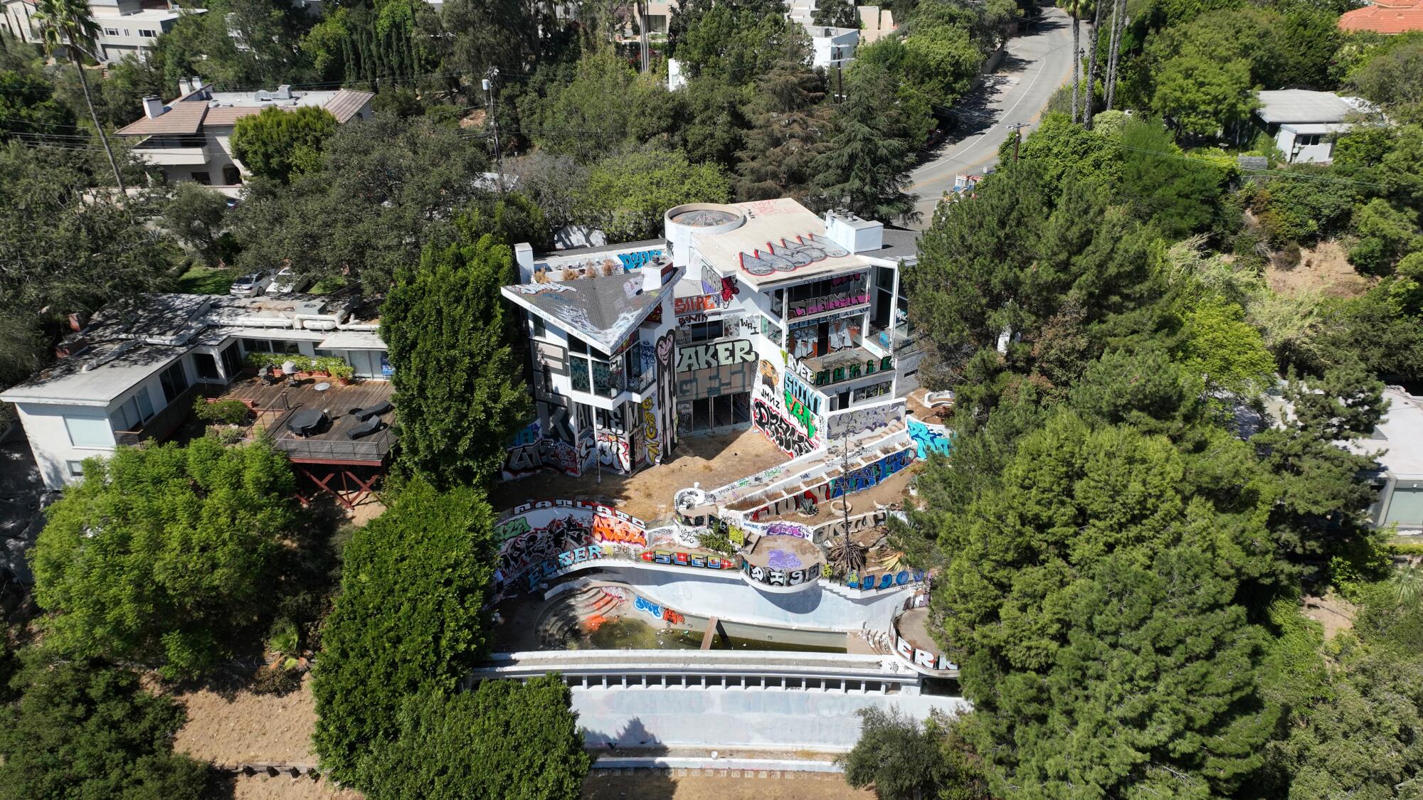 Aerial view of graffitied mansion surrounded by trees and other homes.