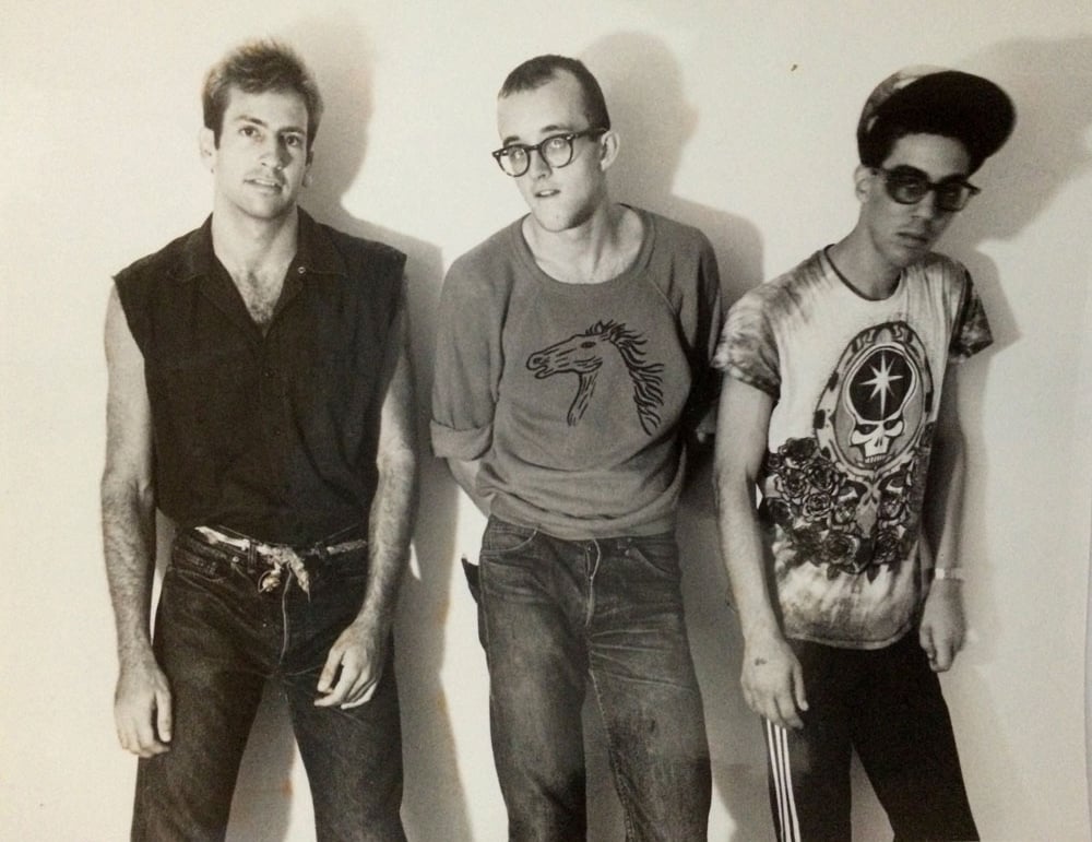 A black and white photo of three young men—Kenny Scharf, Keith Haring, and Futura 2000—in 1980s streetwear fashion.