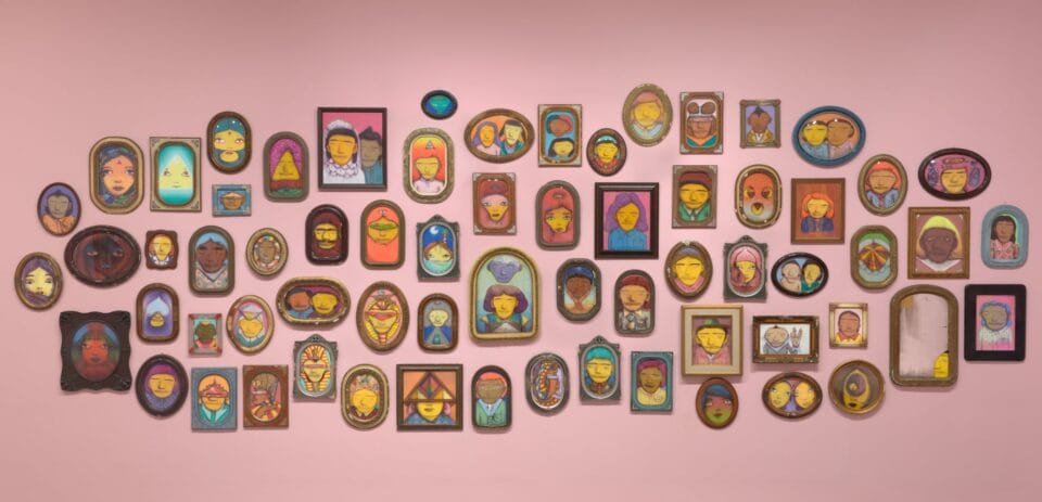 a collection of small framed portraits of yellow figures on a pink wall