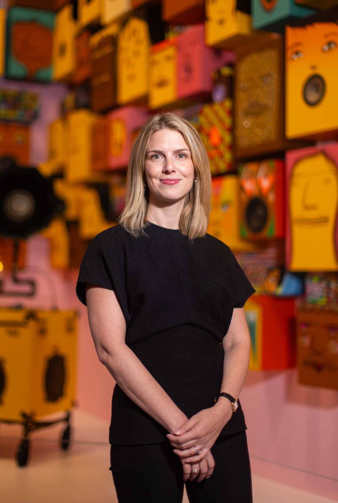 Curator Marina Isgro poses for a portrait in front of a finished portion of the exhibition, with “Gramaphone, 2016” and “ Untitled (92 Speakers), 2019.”