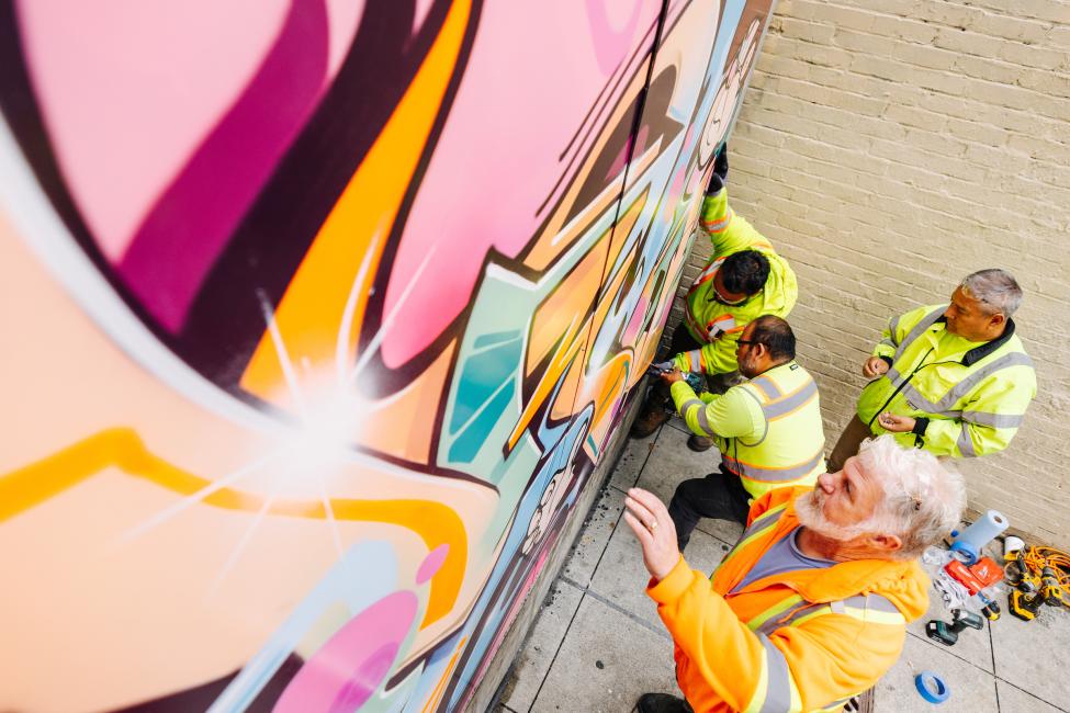 A construction crew installs new graffiti art on a wall