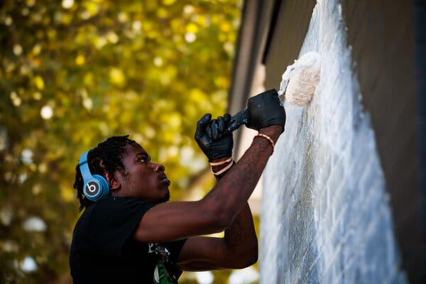 A male artist wearing headphones rolls white paint onto a black wall.