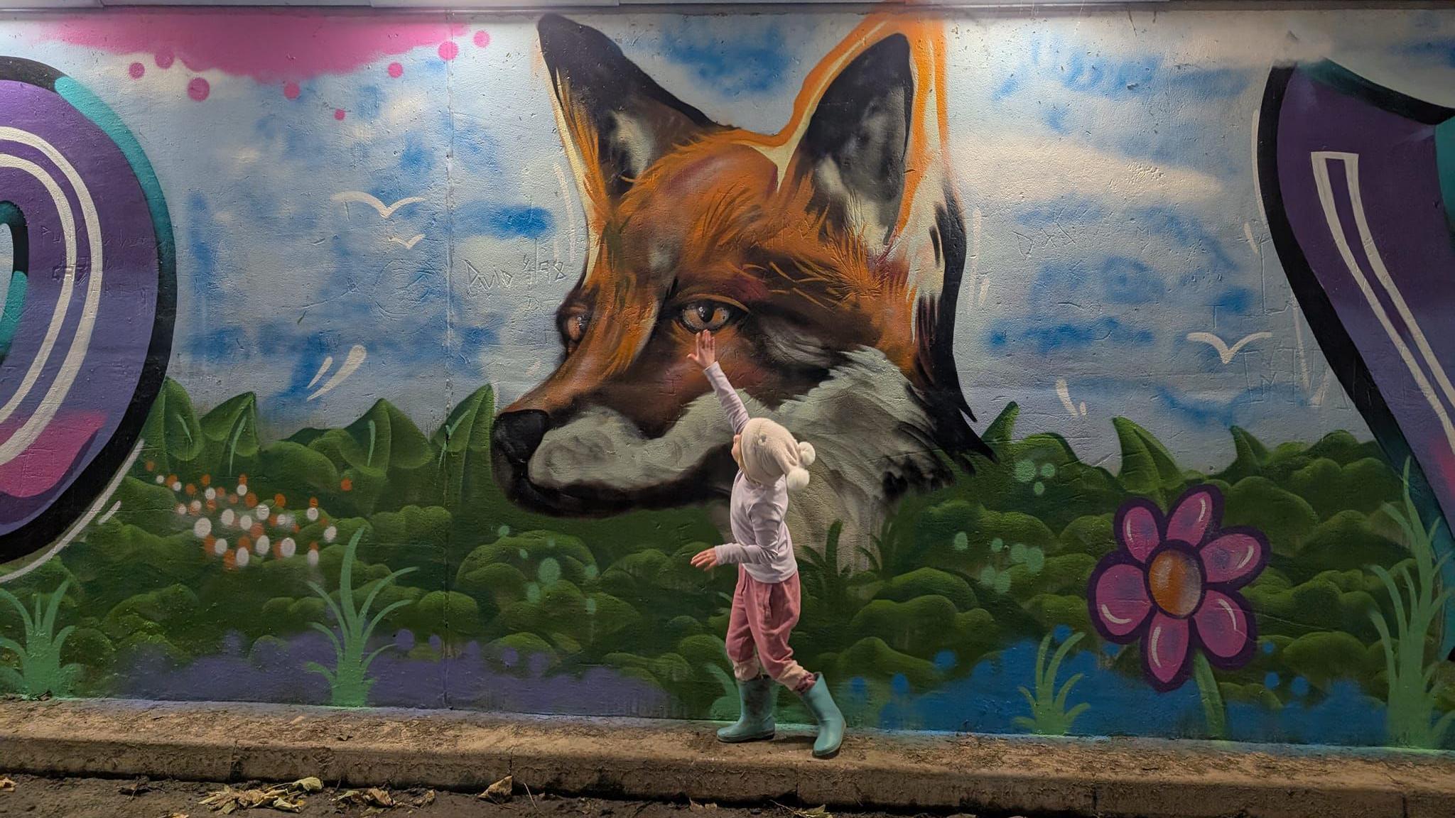 A young girl reaches to touch a painted fox on the subway wall